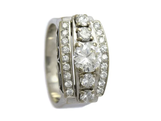 RING, 18K vitguld, briljantslipad diamant ca 0,94 ct, ca H-I(W-TCR/SI (nagg i rondisten) 22 briljantslipade diamanter ca 0,90 ctv, ca TW-W/VS, stl 17,75 mm, Björkman & Magnell, Stockholm 1985, vikt 12,4 g, mittstenen sitter löst i sin fattning, tre av de fyra större sidostenarna är skadade.