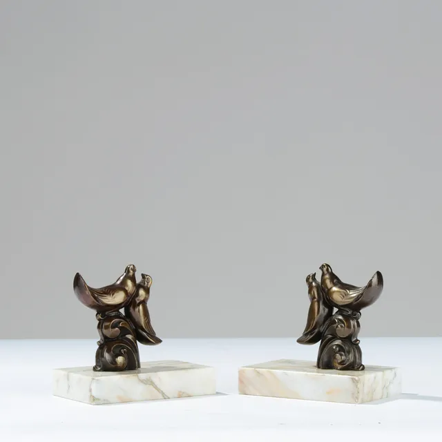 ART DECO: Et par bogstøtter med fugle af bronzepatineret metal på lyse marmorsokler, europæisk formgiver, 1900-tallets midte, (2).