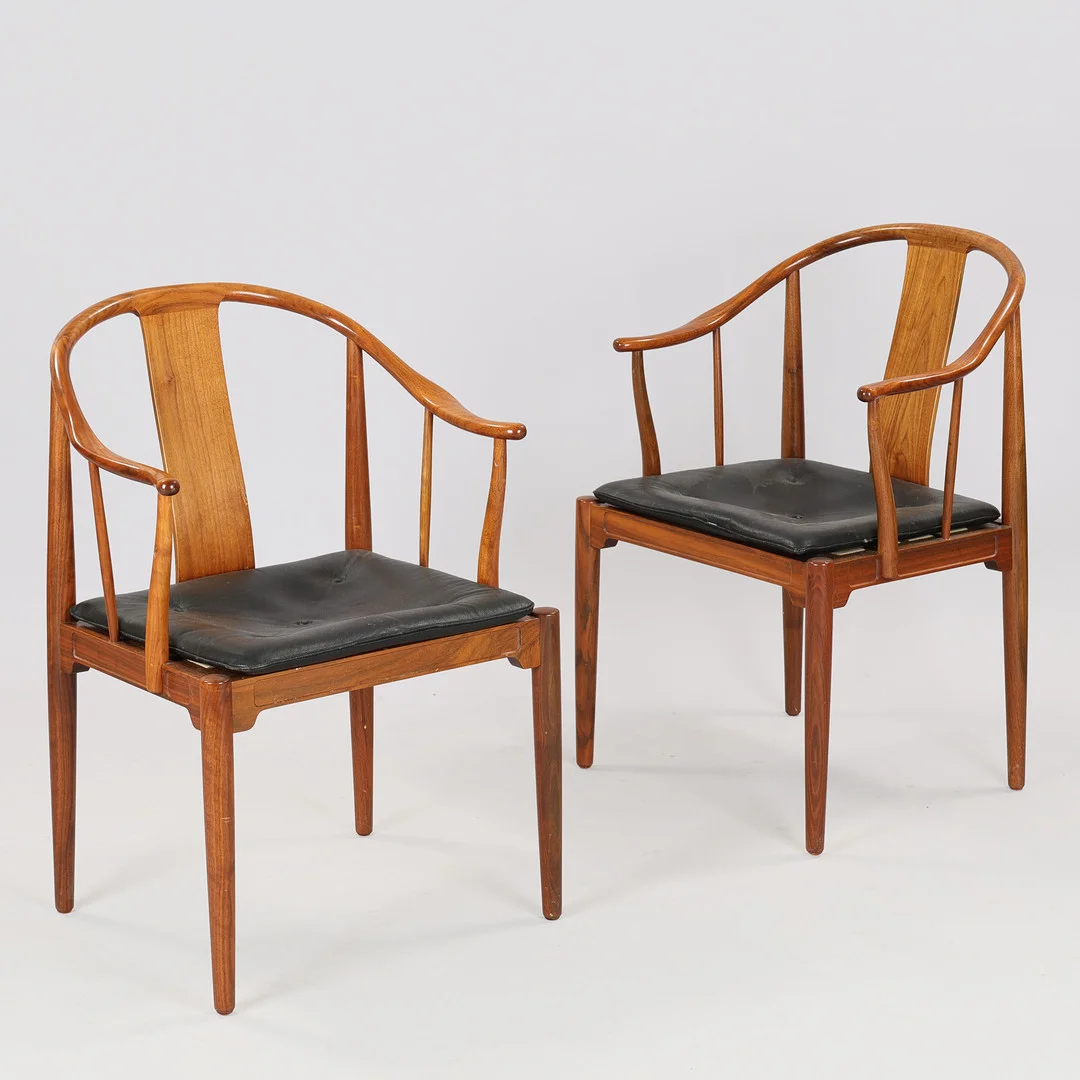 HANS J WEGNER (1914–2007). "Kinastolen", et par armstole af valnød, sædehynde betrukket med sort læder, Fritz Hansen, Danmark, model 4283, formgivet 1944, (2). — Armchairs & Chairs — Palsgaard Kunstauktioner