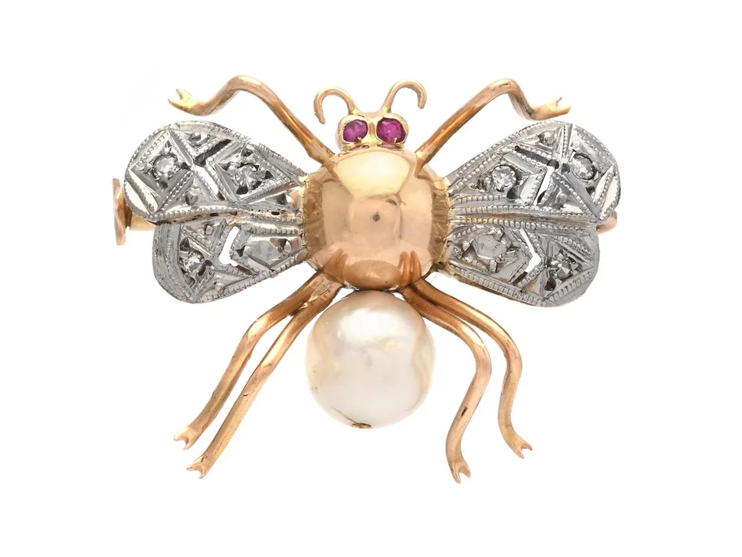 BROSCH, fluga, 18K guld/vitguld, odlad pärla ca 6,9 mm, syntetiska rubiner, åttkantslipade diamanter ca 0,06 ctv, mått 25x20 mm, vikt 4,2 g, två diamanter har skador. — Smycken/Brosch — Kaplans