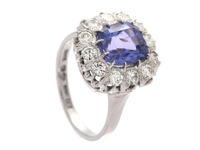 CARMOSÉRING, 18K vitguld, 1 kuddslipad blå safir med lila ton 0,92 ct, enligt gravyr, 12 briljantslipade diamanter ca 0,60 ctv, ca Cr-TCa (J-L)/VS, Stockholm1974, stl 17,25 mm, safir med nagg och mindre skada på rondist, slitna klor och fattningar.
