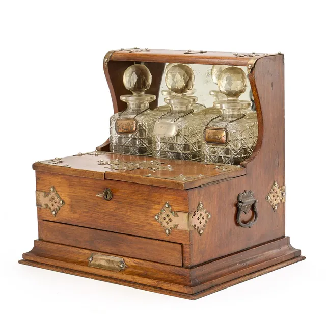 Edwardian tantalus of polished oak with metal fittings, three cut-glass decanters, front with two hinged doors concealing a compartment, narrow drawer below. Early 20th century. H. 35 cm L. 38 cm W. 29 cm.
