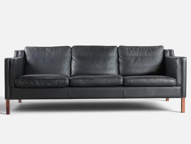 Fritstående tre-personers sofa betrukket med sort skind, ben af massiv bøg. Udført og mærket hos Stouby. Danmark, 20. årh. anden halvdel.