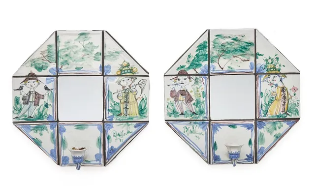 A pair of wall candle sconces with earthenware tiles decorated with a blue-glazed pattern on a light grey base. Fitted with mirrors and mounted on grey-painted chipboard. Signed Bjørn Wiinblad, 71. W./H. 38 cm. D. 12 cm. (2)
