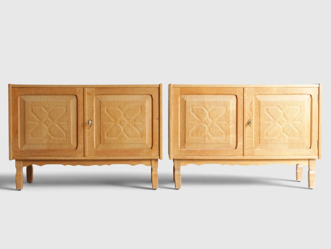 Et par lave skænke af eg, front med låger med udskæringer bag hvilke hylder, tilspidsede ben. Danmark, 1960-70'erne - Henry Kjærnulf-stil (2). — Cupboards, Cabinets & Shelves — Woxholt Auktionshus