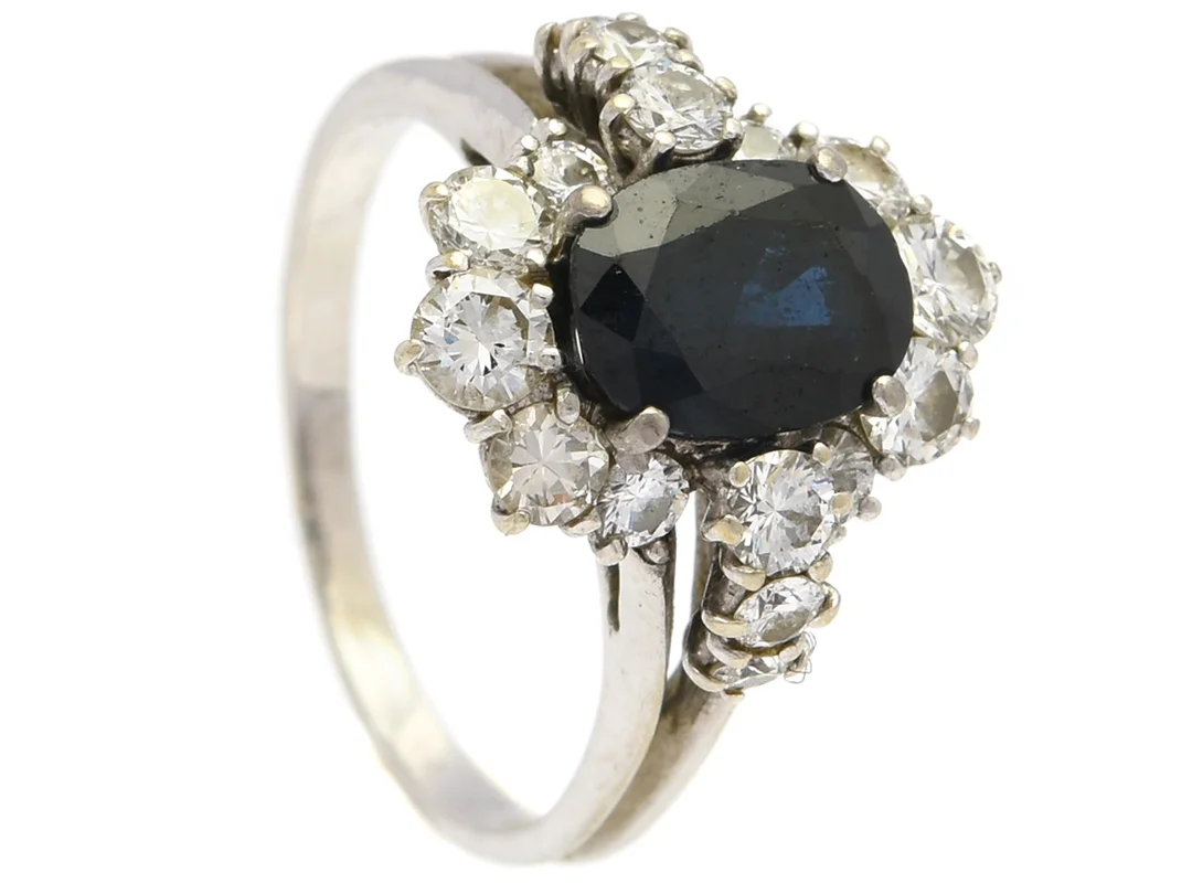 RING, 18K vitguld, blå safir, 16 briljantslipade diamanter ca 0,80 ctv, ca W-TCR/VS-SI, stl 17,5 mm, vikt 4,6 g, spricka i guldet, porösitet i guldet, safir med slitna fasetter, diamanter med nagg och skador. — Smycken/Ring — Kaplans