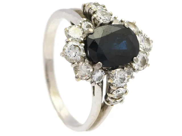 RING, 18K vitguld, blå safir, 16 briljantslipade diamanter ca 0,80 ctv, ca W-TCR/VS-SI, stl 17,5 mm, vikt 4,6 g, spricka i guldet, porösitet i guldet, safir med slitna fasetter, diamanter med nagg och skador.
