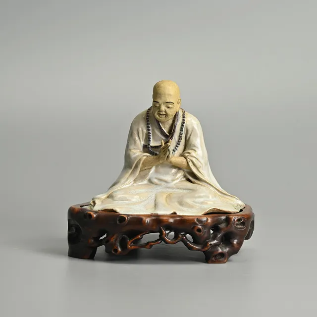 A CHINESE SHIWAN TYPE GLAZED CERAMIC FIGURE OF A MONK ON A CAVRED WOOD BASE, 20TH CENTURY.