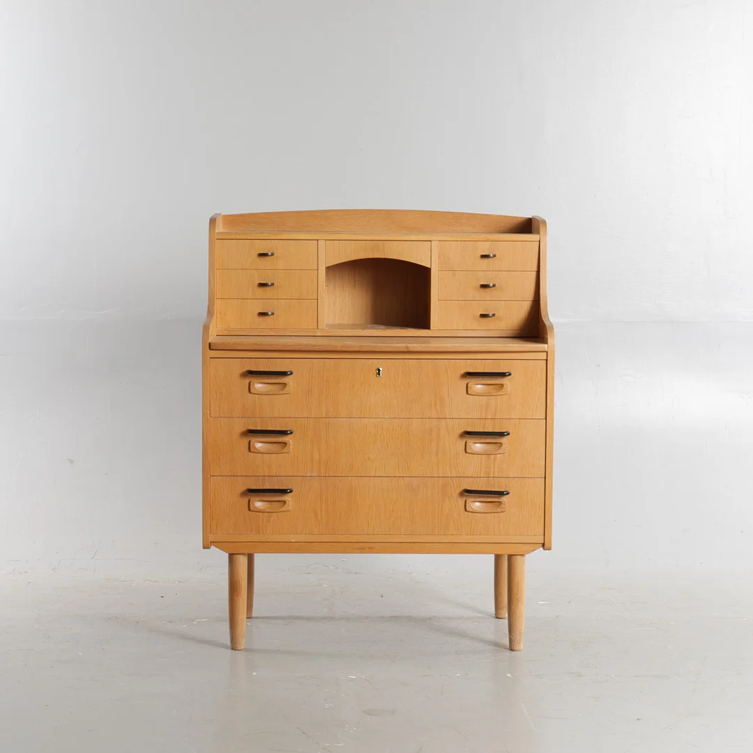 DANSK MØBELDESIGN. Chatol af eg, front med store og mindre skuffer, låge med spejlfelt og udtræksplade, opsat på tilspidsede ben. Danmark, 1960'erne. — Cupboards, Cabinets & Shelves — Woxholt Auktioner