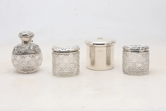 English lidded pot by Godsmiths & Silversmiths, from 1926, and three vanity jars in carved glass and silver.
