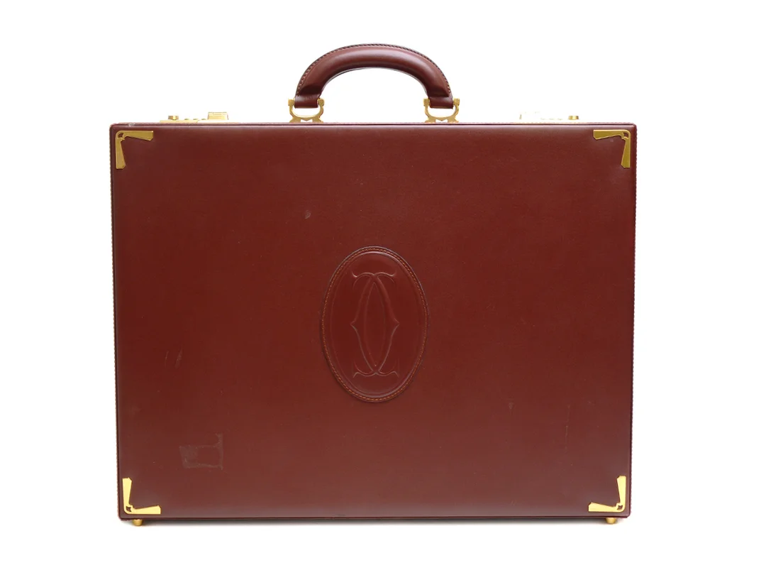 PORTFÖLJ, CARTIER, Must de Cartier, vinrött läder med detaljer i gulmetall, två kodlås, 5 stycken innefack samt mindre fickor, mindre skada och märken, 43x33x9 cm, dustbag (ej orginal). — Accessoarer/Väskor — Kaplans