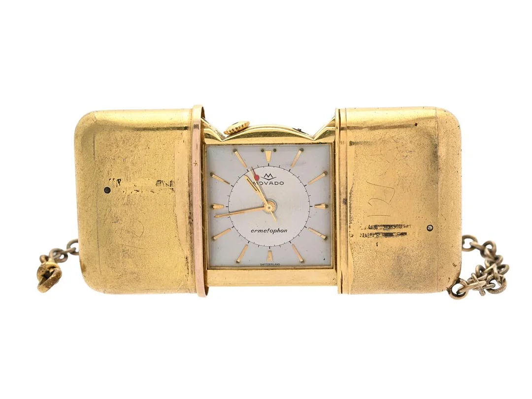 MOVADO, Ermetophon, Boett nr. 312, fickur, 49,5 x 38,5 mm (utfälld 77 mm), gulmetall, manuell, plexiglas, alarm, skadad urtavla, skadad boett (saknar läder), OBS: saknar krona, ca 1960, kedja gulmetall. Klockan dras upp genom att öppna och stänga fodralet. — Klockor/Movado — Kaplans