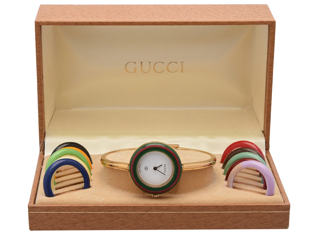GUCCI, damur, 26 mm, Serie nr. 0240734, Boett nr. 1100-L, doublé, quartz, mineralglas, skadad urtavla, 11 st. utbytbara ringar (1 st. missfärgad), integrerad originallänk, längd 160-165 mm, ca 1995, box. — Klockor/Gucci — Kaplans