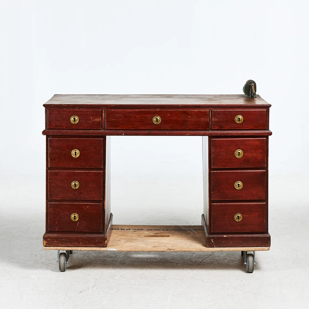 SKRIVBORD. 1900-talets början, furu, rödbetsat, tre draglådor i sarg, vardera hurts med tre draglådor, beslag i patinerad mässing, tidigare monterad pennvässare kvar. — Tables — Stockholms Auktionsverk Sickla