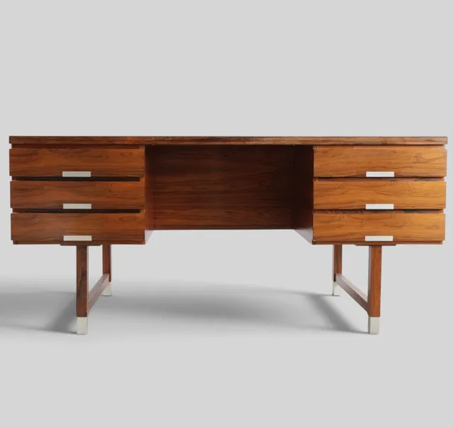 Fritstående skrivebord af palisander, front med seks skuffer, bagside med hyldeinddeling, greb samt sko af aluminium. Udført hos Eigil Petersens Møbelfabrik for Preben Schou. Danmark, 1960'erne.