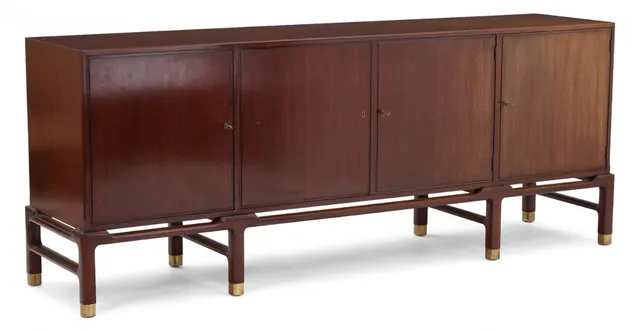 Freestanding mahogany sideboard with patinated brass feet. Profiled front featuring four doors; interior fitted with shelves and pull-out trays. Made by master cabinetmaker William Christensen for Illums Bolighus. H. 85.5 cm. D. 49 cm. L. 214 cm.