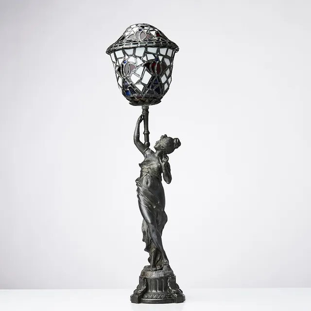 BORDSLAMPA, jugend, i form av kvinna hållandes lampkupa, kupan i blyinfattat glas, runt sekelskiftet 1900.