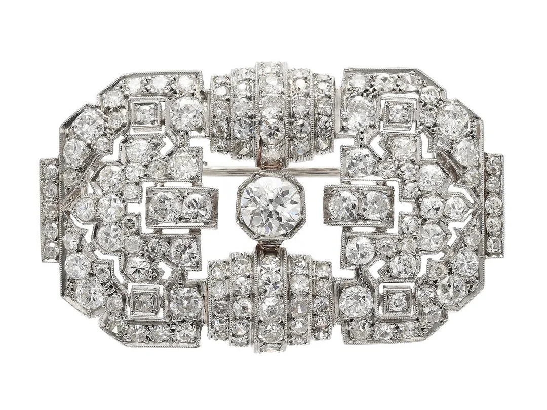 BROSCH, platina, gammalslipad diamant ca 0,82 ct, TCr(I)/P, 186 gammal- och åttkantslipade diamanter ca 5,00 ctv, ca TW-TCr/VS-P, mått 46x29 mm, vikt 18,3 g, några svaga fattningar, mittstenen har små skador och nagg vid rondisten i anslutning till inneslutning som når ytan, flera sidostenar har nagg och skador. — Smycken/Brosch — Kaplans