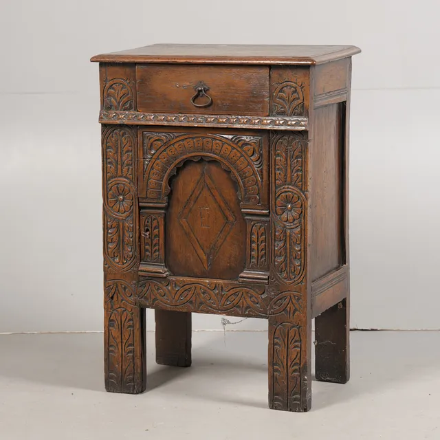 A 17TH CENTURY STYLE CARVED OAK BEDSIDE CUPBOARD.