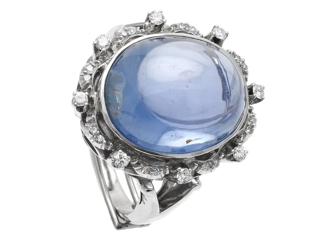 RING, 18K vitguld/platina, cabochonslipad safir ca 25,00 ct, briljant- och åttkantslipade diamanter ca 0,30 ctv, Erik Thomassons Guld & Juvelfirma, Stockholm 1900-talets mitt, stl ca 16,5 mm, vikt 14,8 g, omarbetad, storleksändrande, spricka i en lödning, några diamanter har skador och nagg, etui. — Smycken/Ring — Kaplans