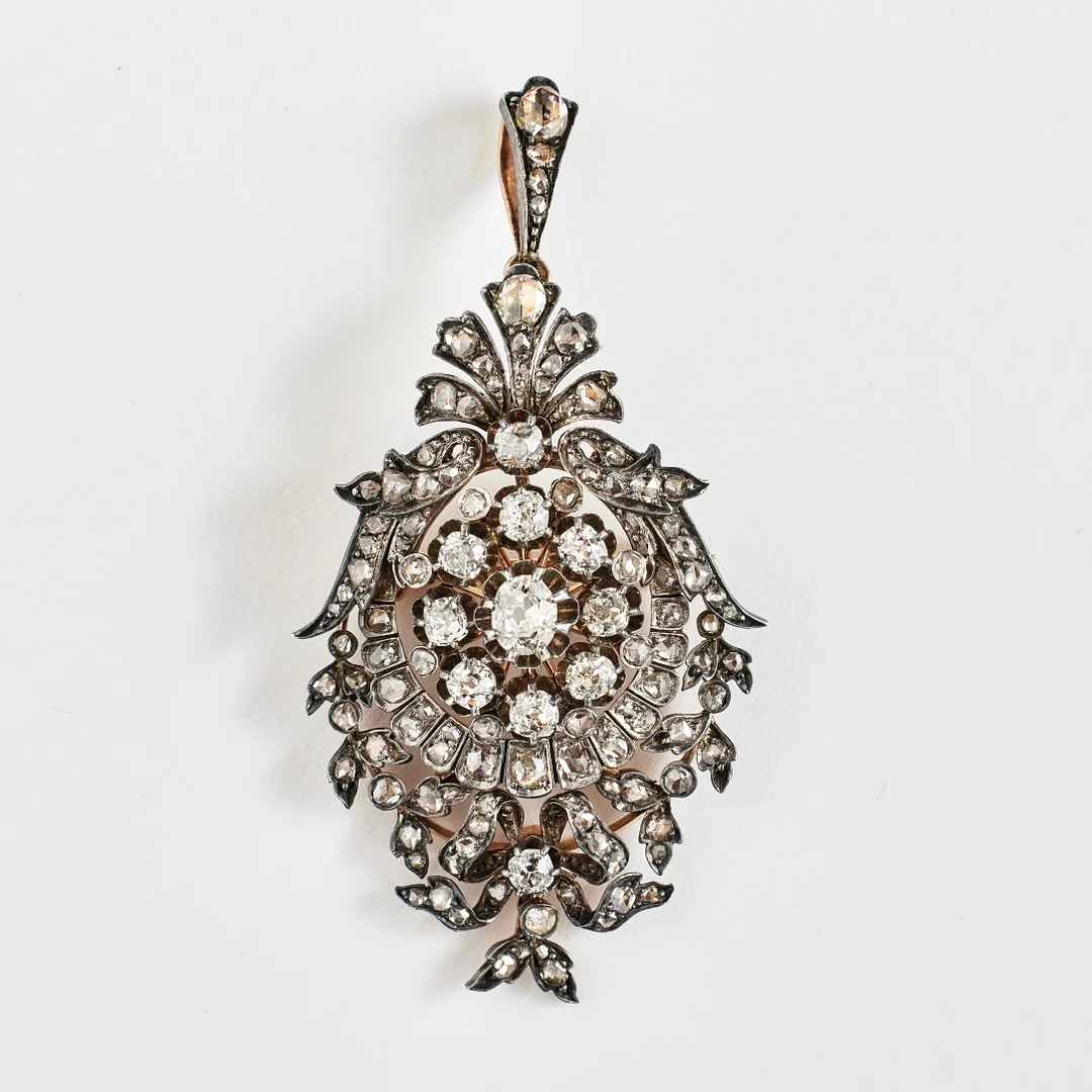 HÄNGE/BROSCH, guld/silver, 1800-talets slut, 1 ovalslipad diamant, ca 0,25-0,30 ct, 10 diamanter med antikslipning, totalt ca 0,12 ct, genombruten dekor med snäckformation, rosett samt bladverk besatta med rosenslipade diamanter. — Brooches & Pendants — Stockholms Auktionsverk Fine Art