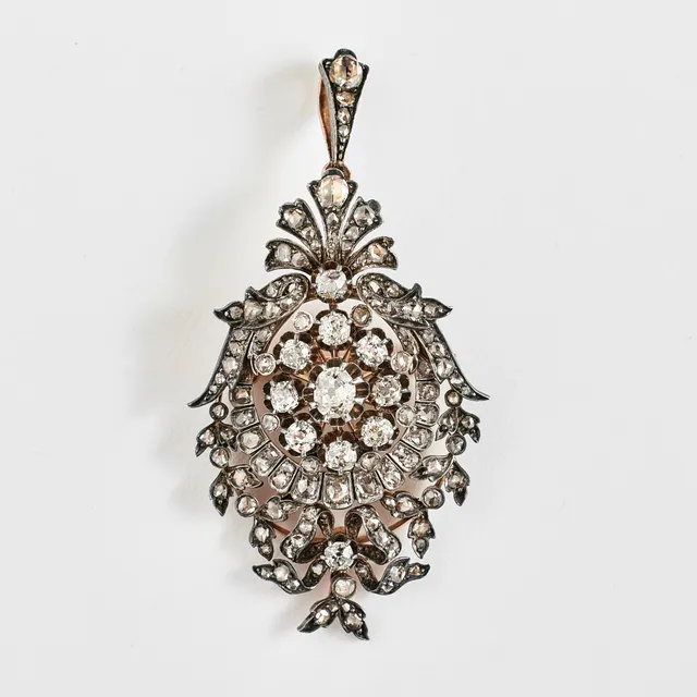HÄNGE/BROSCH, guld/silver, 1800-talets slut, 1 ovalslipad diamant, ca 0,25-0,30 ct, 10 diamanter med antikslipning, totalt ca 0,12 ct, genombruten dekor med snäckformation, rosett samt bladverk besatta med rosenslipade diamanter.