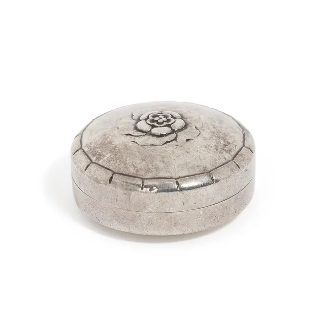 A sterling silver pill-box with slightly hammered surface. Cover with relief flower decor. Georg Jensen after 1945. Design no. 79 D. Weight 18 g. H. 1.8 cm. Diam. 3.7 cm.