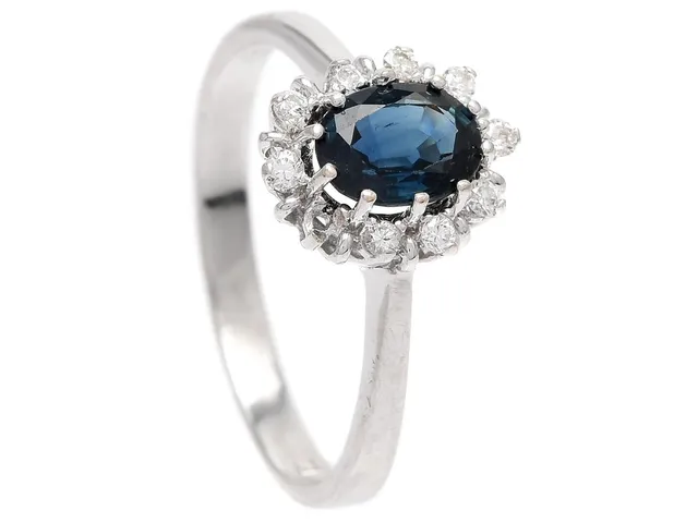 CARMOSÈRING, 18K vitguld, 9 briljantslipade diamanter ca 0,13 ctv, ovalslipad blå safir, stl 18 mm, vikt 3,0 g, en diamant saknas, safiren har nagg och slitna fasettkanter.