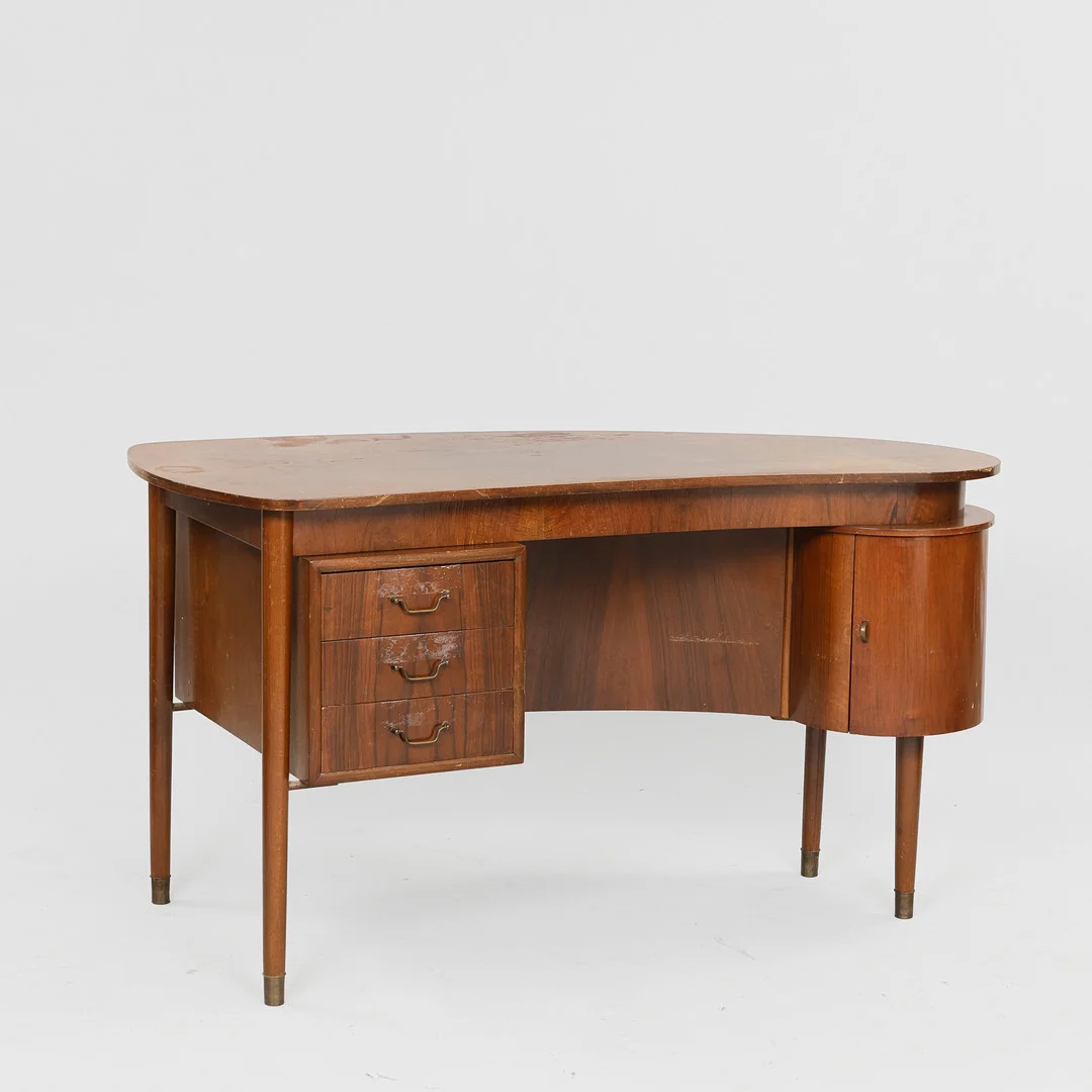 Fritstående nyreformet skrivebord af nøddetræ, greb og sko af messing, antageligt dansk møbelproducent, Danmark, 1950'erne. — Desks — Palsgaard Kunstauktioner