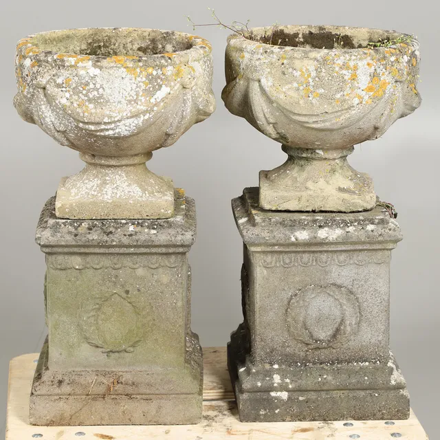 A PAIR OF RECONSTITUTED STONE URN PLANTERS ON PLINTHS.