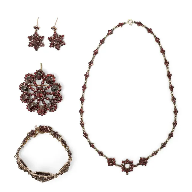 A garnet jewellery set comprising of a pair of ear pendants, brooch/pendant, bracelet and necklace each set with circular-cut and oval-cut garnets, mounted in gilded silver. Ear pendants L. 29 mm. Brooch diam. 5 cm. Bracelet L. app. 16 cm. Necklace L. 40 cm. (5)