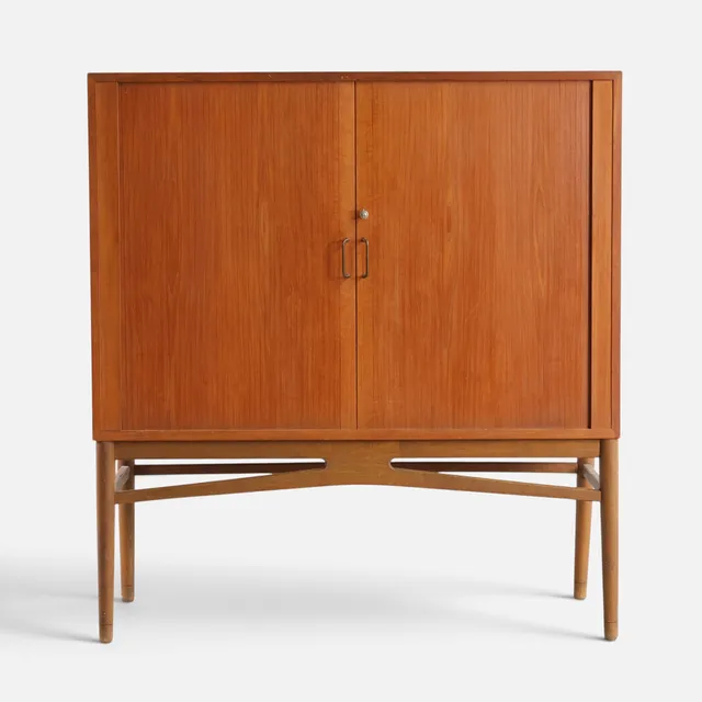 Arkivskab af teak, front med jalousilåger bag hvilke udtræksbakker, stel af eg med tilspidsede ben, afsluttende på 'sko', greb af messing. Danmark, 1950-60'erne.